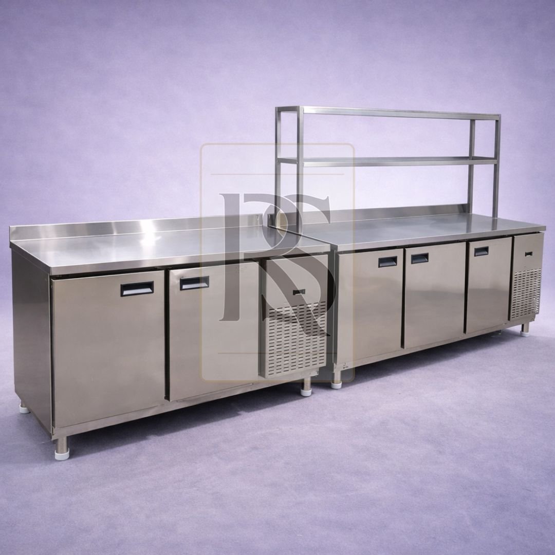 The Versatile Foundation of High-Performance Kitchens Our Customised Under-Counter Chiller is engineered to turn dead space into a high-utility cold storage hub. By integrating a powerful refrigeration system directly into your prep table, we reduce the need for chefs to walk to walk-in coolers, significantly speeding up service times. Whether you need a 2-door, 3-door, or a multi-unit setup with overhead pick-up shelves, these chillers provide the thermal stability and industrial durability required for 24/7 commercial use. Key Features & Benefits: Dual-Functionality Design: Serves as a heavy-duty stainless steel prep table and a high-performance reach-in chiller, maximizing every square inch of your kitchen. Customisable Overhead Shelving: (Visible in image) Options to add reinforced stainless steel overhead racks for storing dry goods, spices, or prep containers, further increasing your storage density. Tropicalized Refrigeration Technology: Equipped with a high-efficiency, side-mounted compressor (Visible in image) designed to maintain consistent temperatures (+2°C to +8°C) even in ambient kitchen heat up to 43°C. Premium SS 304/202 Fabrication: Built with food-grade brushed stainless steel inside and out for maximum hygiene, rust resistance, and a surface that is exceptionally easy to sanitize. Precision Digital Thermostat: Features a micro-computer controller with an external LED display for real-time temperature monitoring and easy adjustments. Self-Closing Doors with Magnetic Gaskets: Designed with heavy-duty hinges and high-quality magnetic gaskets to ensure a perfect seal every time, reducing energy consumption and frost buildup. Reinforced Worktop: The top surface is reinforced with industrial-grade under-padding to handle heavy kitchen equipment, dough kneading, and chopping without warping. Adjustable Bullet Feet: Mounted on reinforced stainless steel legs with levelers to ensure a rock-solid, even work surface on any kitchen floor. Technical Specifications: Material: Grade 304/202 Industrial Brushed Stainless Steel Configuration: 2-Door, 3-Door, or 4-Door models available Temperature Range: +2°C to +10°C (Adjustable Chilled Performance) Compressor: High-Efficiency Side-Mounted Unit for easy maintenance Shelving: Adjustable Internal Wire Racks + Optional External Overhead Racks Legs: Heavy-Duty Stainless Steel Adjustable Bullet Feet Dimensions: Custom Built per client layout (Typical: 4ft to 8ft Length x 30" Width x 34" Height)